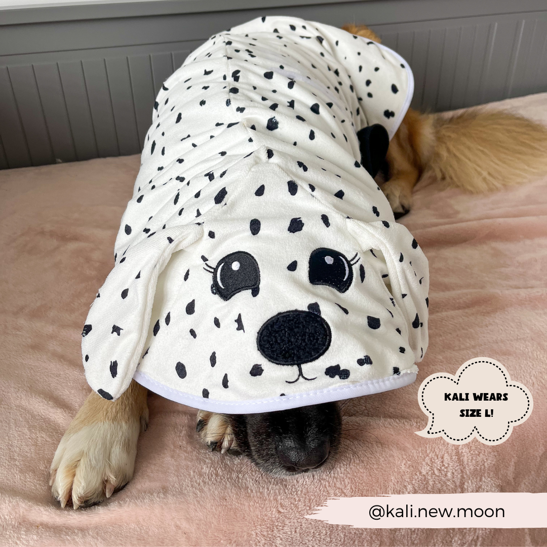 A dog is lying down, covered in a Dalmatian Drying Robe from Cocopup London, designed to look like a Dalmatian puppy. The Premium Microfibre blanket features cartoon eyes, nose, and ears. Text on the image reads: "KALI WEARS SIZE L!" and "@kali.new.moon".