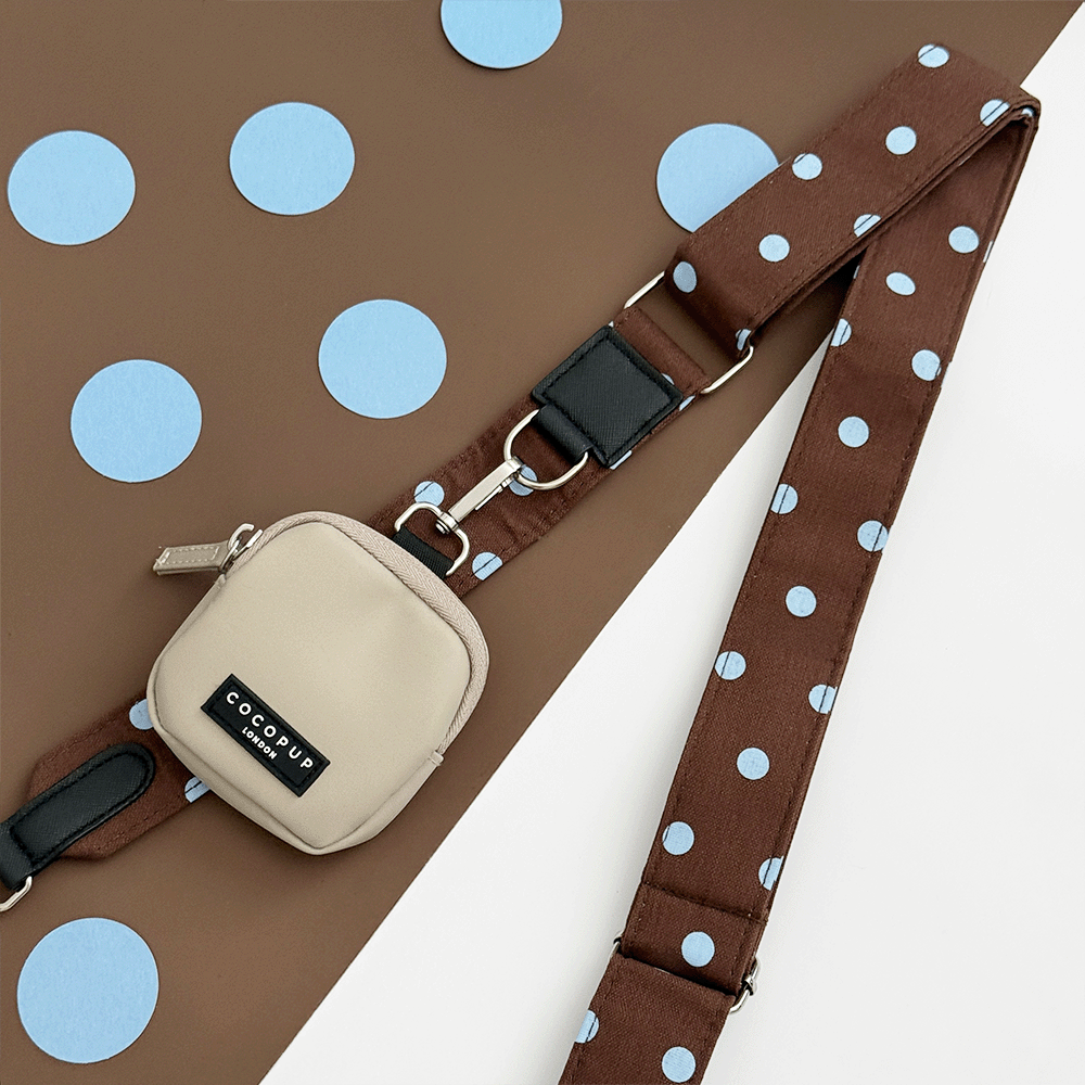 A brown bag strap with light blue polka dot design. Attached is a beige small pouch for dog treats.