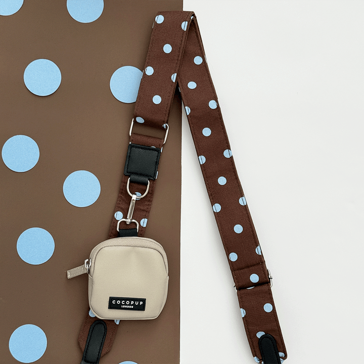 A brown bag strap with light blue polka dot design. Attached is a beige small pouch for dog treats.