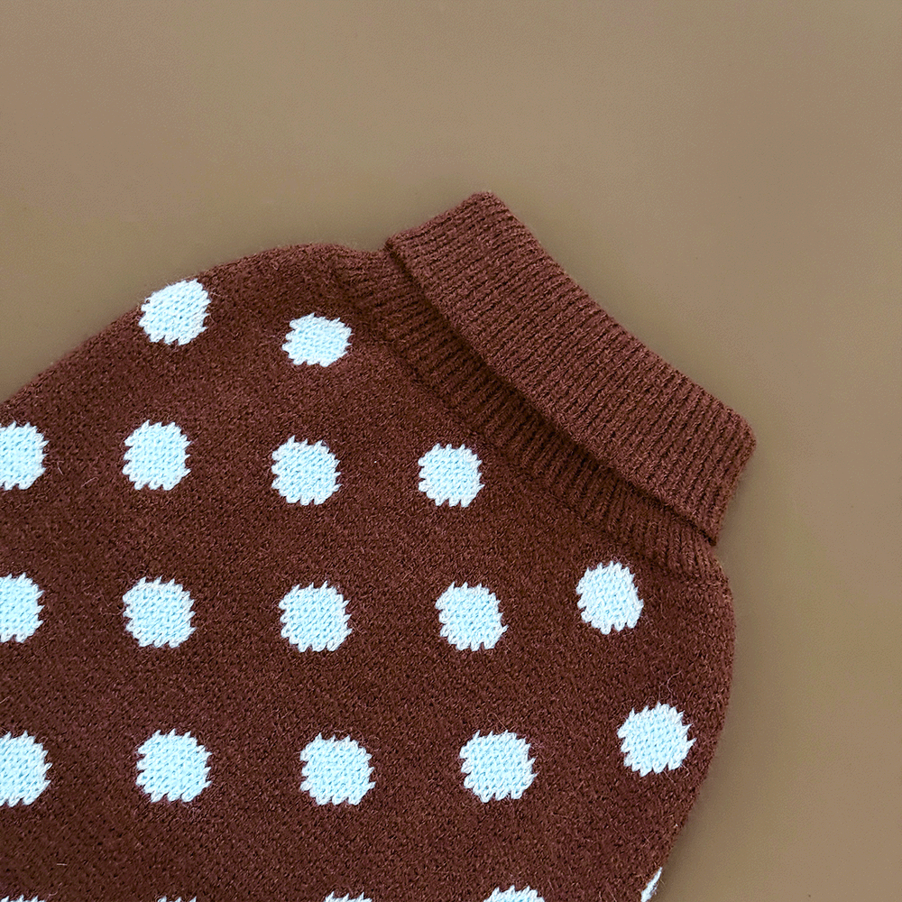 A close-up of a brown knit dog jumper with pale blue polka dots, showing the ribbed collar, on a solid beige background.