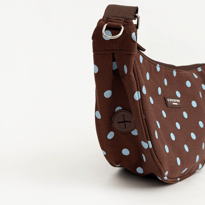 A brown fabric crossbody bag with a light blue polka dot pattern. Featuring Cocopup London logo badge and plain brown strap.