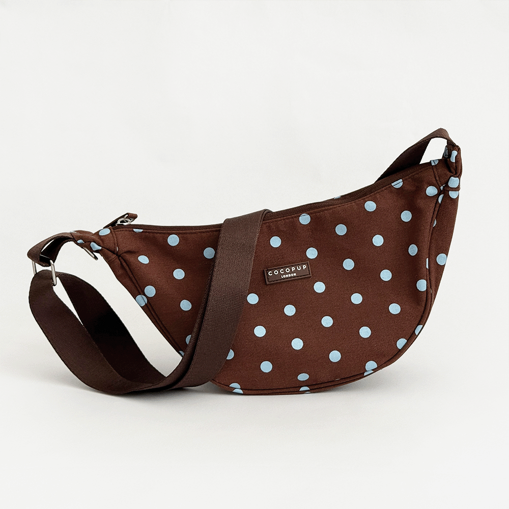A brown fabric crossbody bag with a light blue polka dot pattern. Featuring Cocopup London logo badge and plain brown strap.