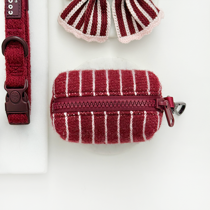 Knitted dog poop bag dispenser with burgundy and baby pink vertical stripes and a colour matched zip closure.