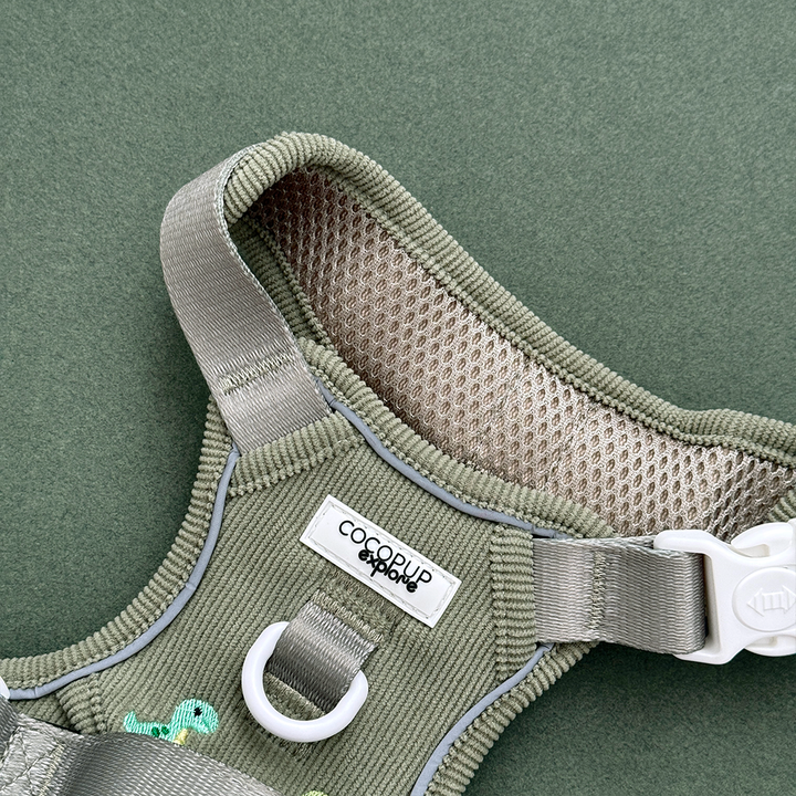 Dog harness in green corduroy material, with embroidered dinosaur design.