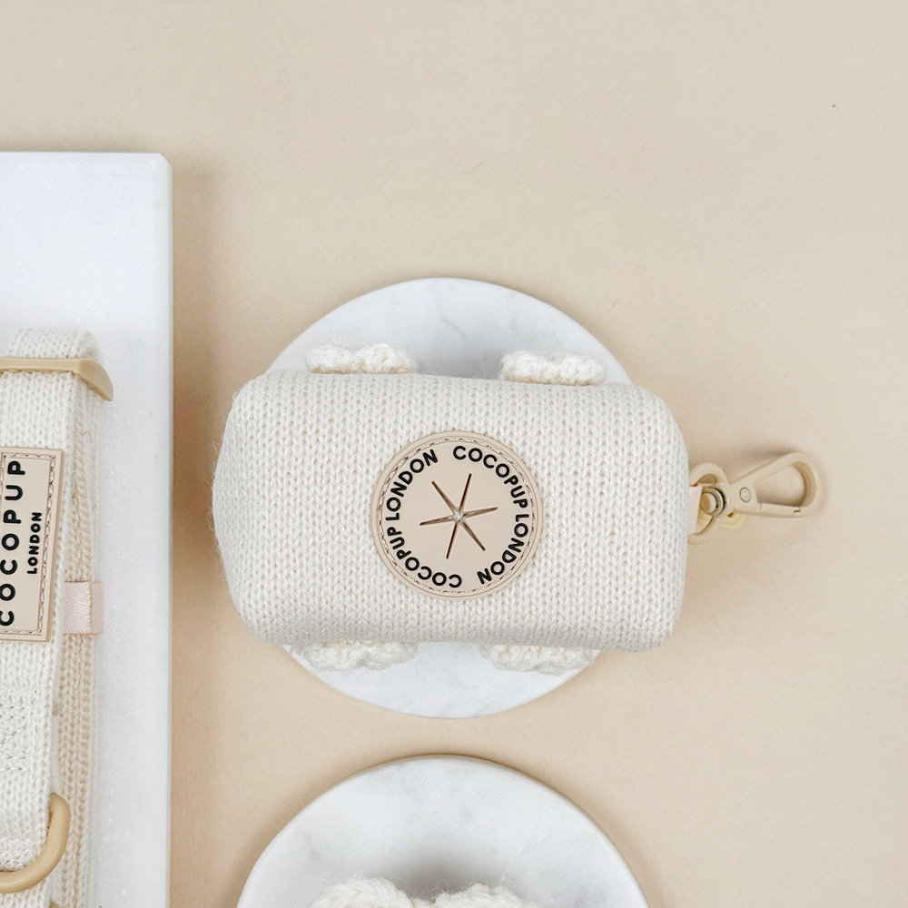 Beige knitted pouch with beige metal clip and hole to put poop bags through.