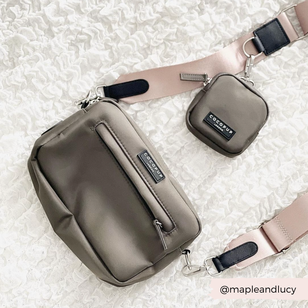 A beige crossbody bag, named the "Dog Walking Bag - Mocha" by Cocopup London, paired with a smaller matching pouch against a white textured background. Both items feature beige straps with black and metal accents and display the brand label "Cocopup." This perfect dog walking bag includes a discreet poop bag dispenser. The handle is labeled with "@mapleandlucy".