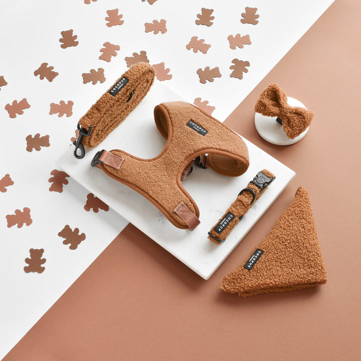 A flat lay photo features the Teddy Paddington Adjustable Neck Harness, Lead & Collar Bundle by Cocopup London. The set, which includes a matching harness, collar, leash, bow tie, and bandana in a charming brown teddy bear-textured fabric, is attractively arranged on a white surface with a speckled bear print and complemented by a brown background.